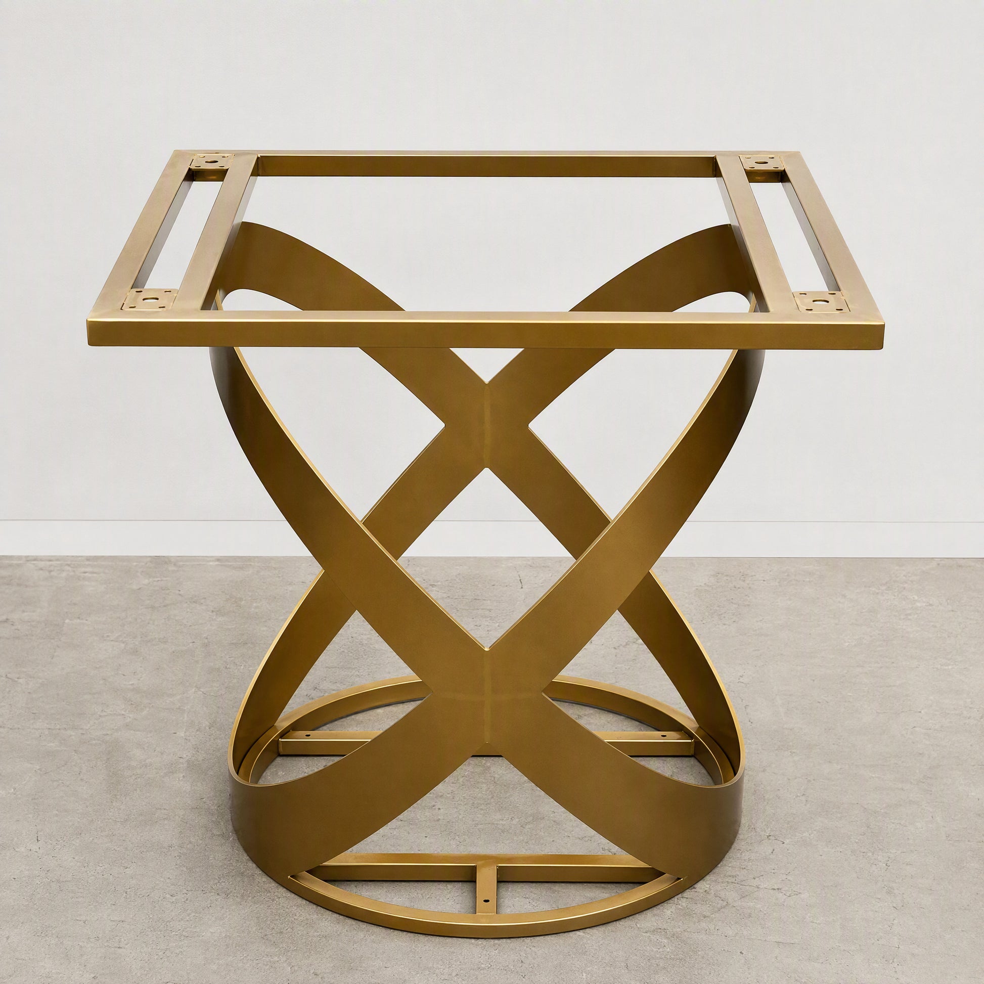 A modern square side table with a gold-finished metal frame and an open, sculptural base made of interlocking curved bands, shown on a light gray concrete floor against a white wall.