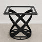 A black metal table base with a square top frame and an interlocking twisted X-shaped pedestal base, shown against a neutral studio backdrop.